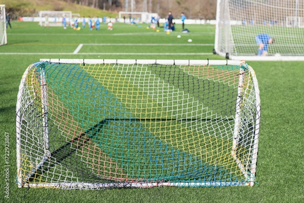 Fototapeta Soccer goal on a sunny day at a youth sports field with players practicing in the background