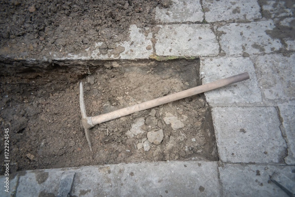 Fototapeta Construction site showing excavated area with a pickaxe resting on the ground