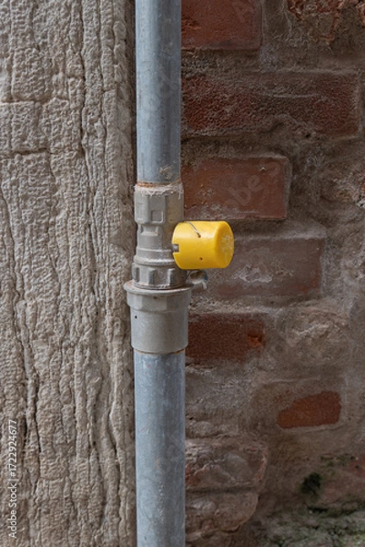 Fototapeta Pipeline fitting with yellow cap and brick wall background in urban setting