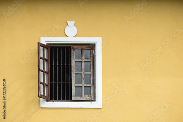 Fototapeta Open window with iron bars in a yellow traditional European style house