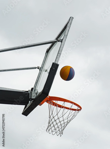 Fototapeta Basketball soaring towards the hoop under a cloudy sky during a casual game in a city park