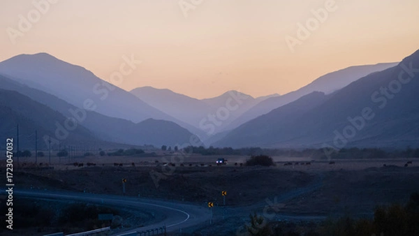 Fototapeta The winding road goes somewhere into the distance, mountain peaks are visible in the distance, twilight, evening panorama of the mountain crevice and the road ahead