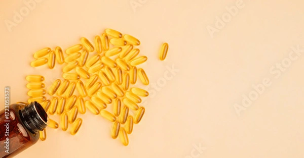 Fototapeta Fish oil softgels spilled from an amber bottle on a beige background with copy space. High quality photo