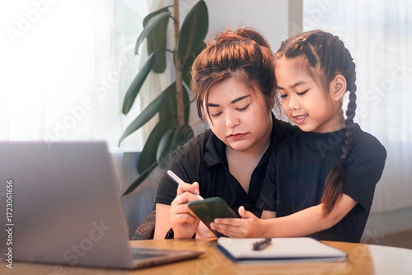 Obraz Mother and daughter working together on a digital device at home during daytime