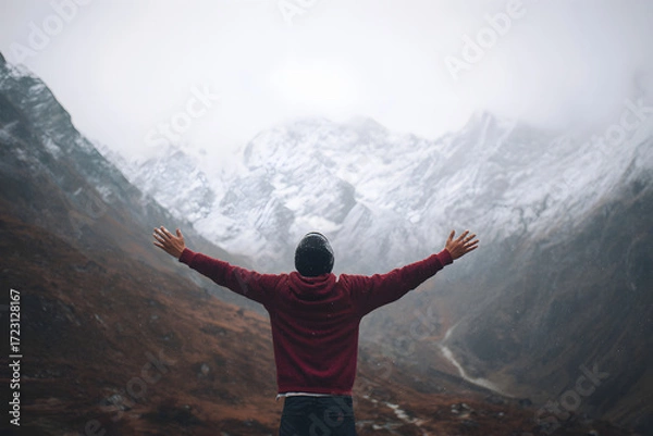 Fototapeta Man with arms wide open facing snowy mountains. Lifestyle image symbolizing freedom and adventure
