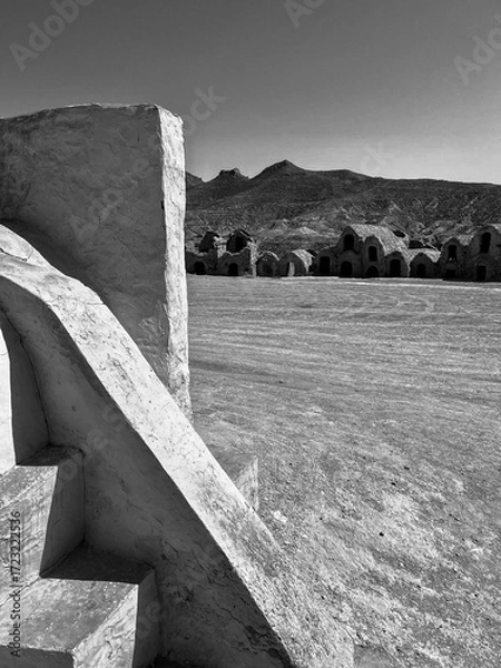 Fototapeta Visitors explore Ksar Ouled Soltane in Tunisia, known for its traditional desert homes used in Star Wars films. The sun shines brightly over the sandy landscape and ancient structures.