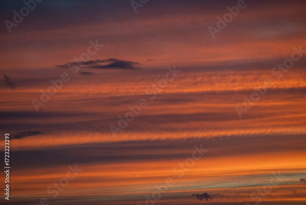 Fototapeta Colors blend beautifully in the sky as the sun rises, casting warm tones of orange and yellow through fluffy clouds.