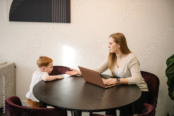 Fototapeta Mother working from home with kid. Quarantine and closed nursery school. Distance learning through war. Child make noise and disturb woman work. Homeschooling and freelance job. Stay at home.