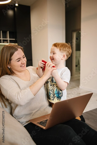Fototapeta Kid make noise and disturb woman working talking on phone. Mom work on laptop from home with child. Homeschooling and freelance job. Quarantine and closed nursery school. Distance learning through war