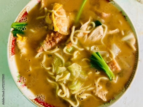 Fototapeta Close-up of a hot bowl of noodle soup served with vegetables, meat, and egg in a savory broth