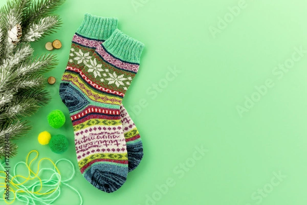 Fototapeta Colorful knitted socks on a green background. Warm socks and a spruce branch symbolize winter comfort. There's space for text.