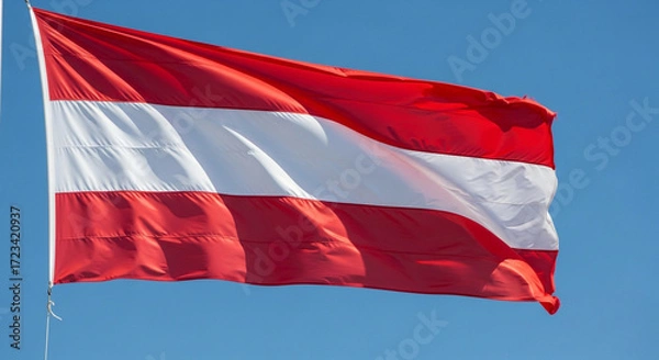Fototapeta Proud Austrian flag waving gently against clear blue sky, symbolizing national pride and vibrant European culture on a sunny day, perfect for travel