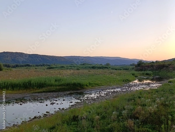 Fototapeta Sunset over a serene river landscape with rolling hills and lush greenery at twilight