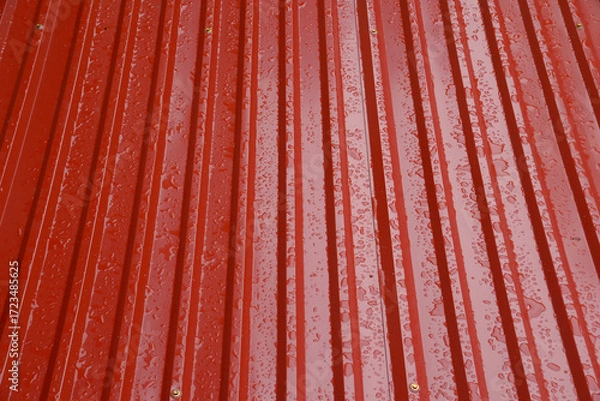 Fototapeta Close-up view of a red corrugated metal roof with raindrops scattered across the surface, highlighting texture and reflections after a light rain in Vietnam