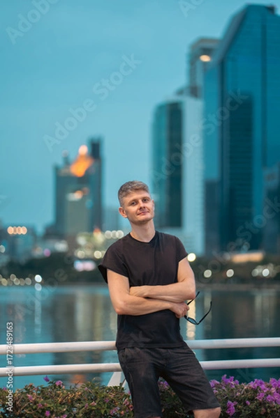 Fototapeta handsome man on vibrant night city with skyscrapers background, stylish guy posing with glowing urban skyline at evening