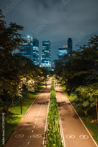 Fototapeta skyscrapers of night Bangkok city with Benchakitti park tracks, illuminated pathways and walkways with people walking and jogging, harmony of bustling city and nature