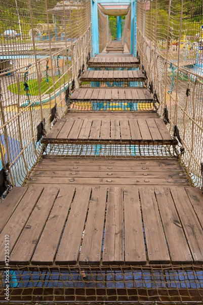 Fototapeta a suspended rope bridge with wooden planks stretches across the playground