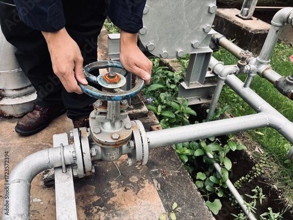 Fototapeta Engineer operating industrial valve on pipeline system in outdoor facility.