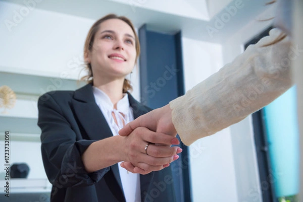 Fototapeta Professional woman in black suit shakes hands with another person in modern office setting, conveying sense of collaboration and agreement. atmosphere is positive and welcoming.