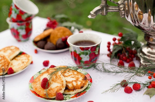 Obraz Самовар с чашками и десертом с малиной на столе в саду. Завтрак на природе 