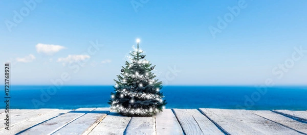 Obraz Geschmückter Weihnachtsbaum auf einem weissen Holzdeck vor einem Blauen Meer