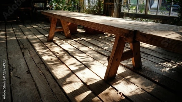 Fototapeta Rustic wooden bench inside a cozy greenhouse with sunlight filtering through glass windows and casting shadows on the weathered wooden floor and furniture
