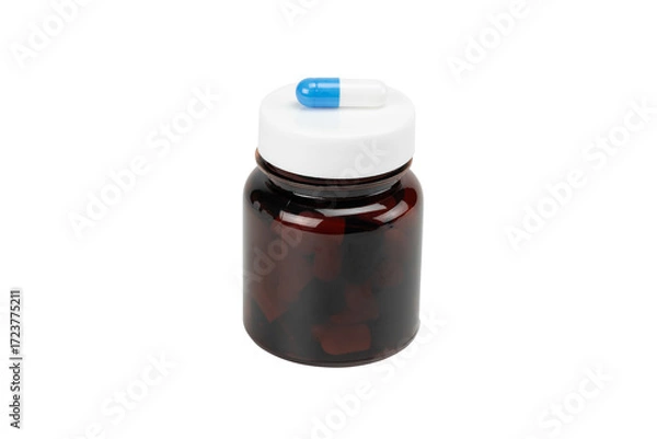 Fototapeta Blue and white pill capsule on the white lid of an amber medicine bottle. Concept of daily dosage, medication schedule, and treatment, isolated on white background with clipping path.