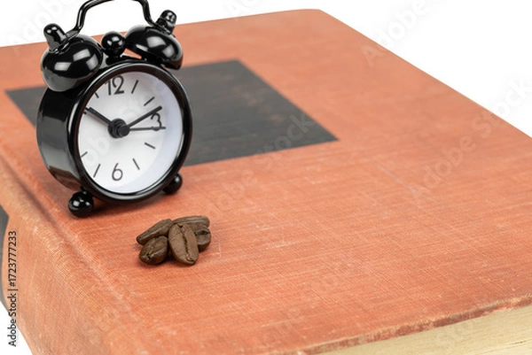 Fototapeta Black alarm clock and coffee beans on an old book, signifying an intense study session or working late to meet a deadline isolated on white background with clipping path.