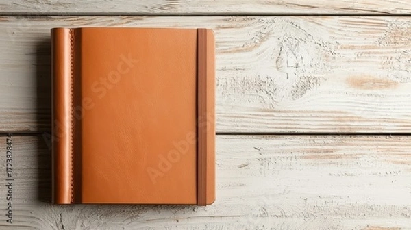 Fototapeta A sleek, brown leather notebook rests on a rustic wooden surface, showcasing a warm, inviting aesthetic for writing or journaling.