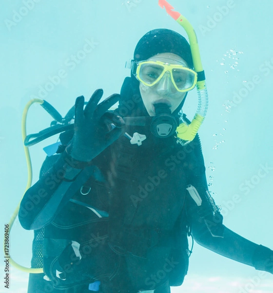 Obraz Scuba diver is signaling OK underwater with yellow diving mask and regulator in turquoise pool