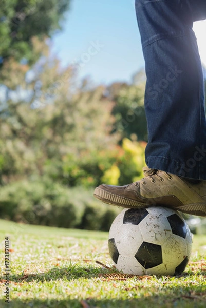 Fototapeta Lower legs in dark blue jeans and tan sneakers pressing soccer ball on sunlit grassy field