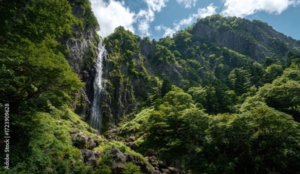 Obraz Mountain waterfall cascading down a rocky cliff face, lush green forest surrounds it