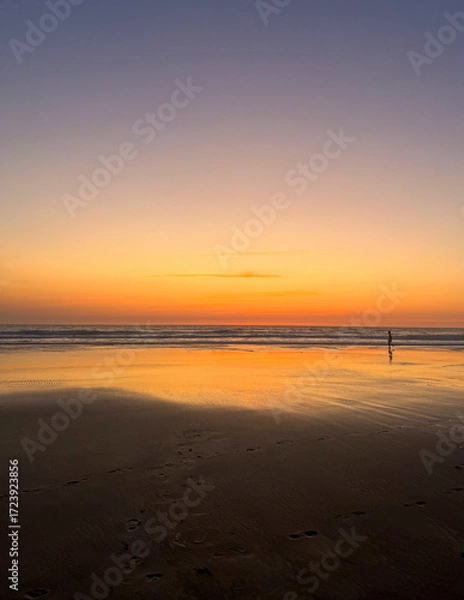 Fototapeta Children play on the sandy shore of Biscarosse as the sun sets, painting the sky in warm hues. The calm waves gently lap at their feet, creating a peaceful atmosphere.