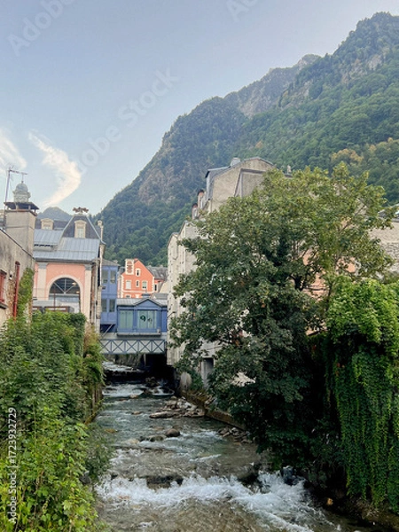 Fototapeta A tranquil scene shows a clear stream flowing over rocks in Cauterets, Pyrenees. Lush green trees surround the area under a clear blue sky, capturing the beauty of nature.