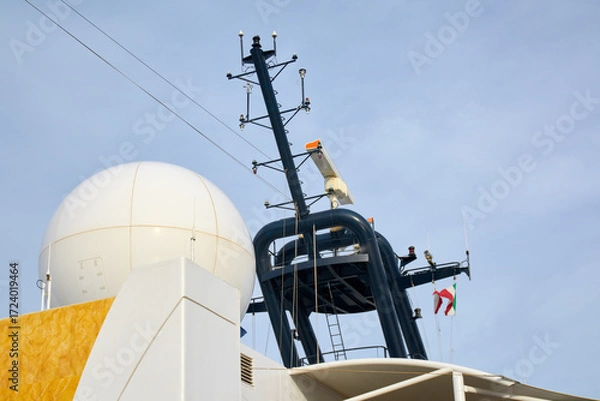 Fototapeta A close-up of the navigation and communication mast of a modern vessel, featuring a large satellite radome, radar scanner, and antennas against a sky.