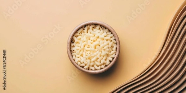 Fototapeta A wooden bowl filled with uncooked elbow macaroni pasta sits on a beige background with textured fabric