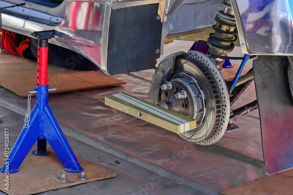 Fototapeta Wheel alignment and camber check on a car, with measuring tool attached to the brake disc and suspension visible during maintenance work.