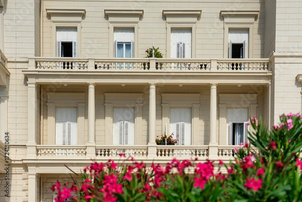 Fototapeta Elegant neoclassical building facade with balconies, shutters, and blooming flowers
