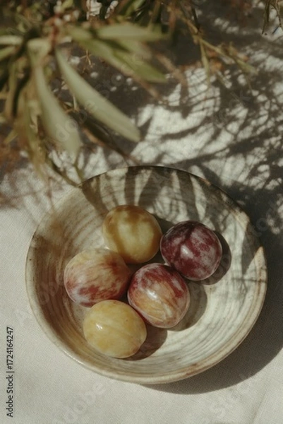 Obraz A ceramic bowl with ripe summer plums sits under dappled olive tree shadows on a linen tablecloth — pure slow living aesthetics.
