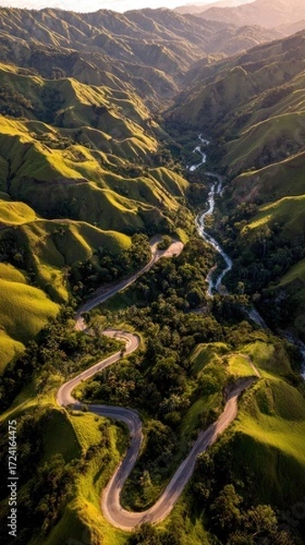 Obraz A winding road snakes through a valley of rolling hills, bathed in golden sunlight, creating a serene and picturesque landscape.