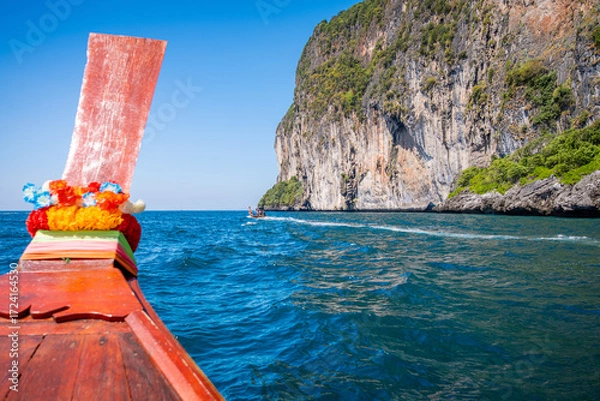 Fototapeta Longtail boat navigating tropical turquoise sea near a towering limestone cliff on Ko Phi Phi Don, offering a unique perspective of this iconic Thai island destination