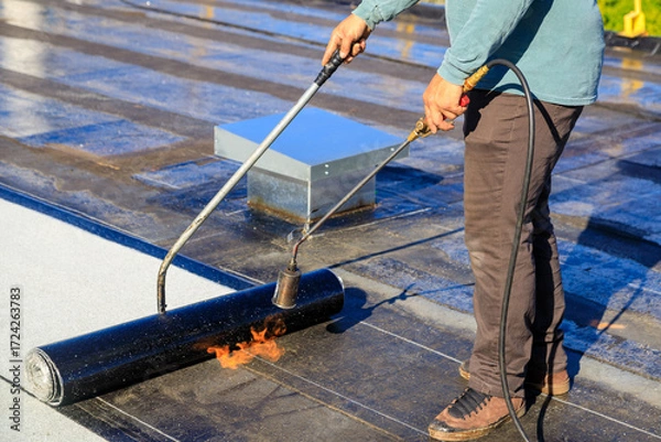 Fototapeta Roofer applying torch to bitumen membrane on torch down roof