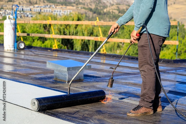 Fototapeta Roofer applying torch to bitumen membrane on torch down roof
