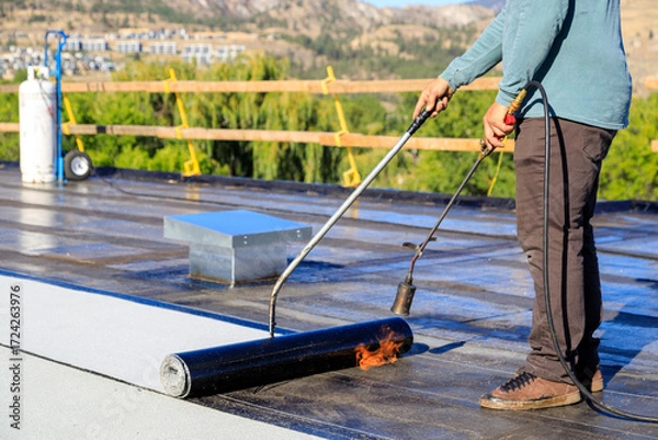 Fototapeta Roofer applying torch to bitumen membrane on torch down roof