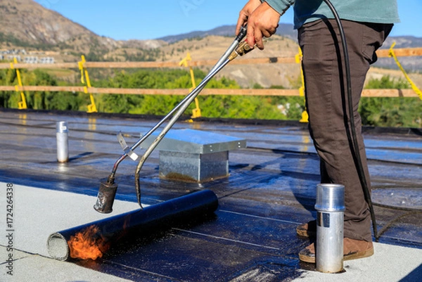 Fototapeta Roofer applying torch to bitumen membrane on torch down roof