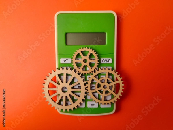 Fototapeta Top view green calculator accompanied by three wooden gears on an orange background