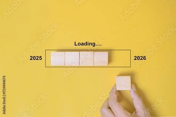 Fototapeta Loading Progress Bar from 2025 to 2026 with Wooden Blocks. A hand places wooden blocks in a row, creating a progress bar transitioning from 2025 to 2026, symbolizing the new year and future progress
