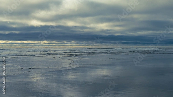 Fototapeta Side view from a wet beach with small waves rolling in, out westward towards the pacific ocean, under a majestic and complicated cloud-scape on a summer day