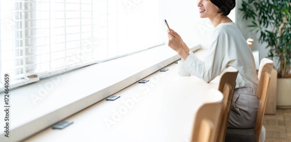 Fototapeta 窓際に座り携帯を触る女性