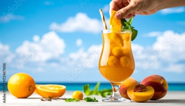 Fototapeta A hand garnishes a large iced cocktail with orange slice and mint,  surrounded by peaches, oranges, and a beach scene